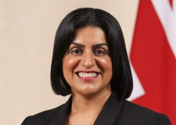 Head-and-shoulders official portrait of a UK home secretary wearing a black suit jacket, with the Union flag behind her