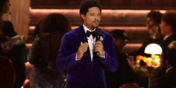 South African comedian Trevor Noah speaking on stage while hosting the 68th Annual Grammy Awards in Los Angeles, wearing a purple velvet tuxedo and holding a microphone
