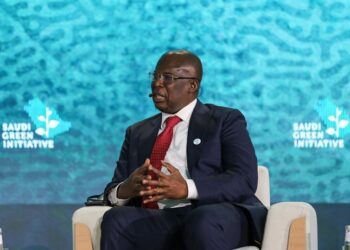 Timipre Sylva speaking on stage at the Saudi Green Initiative forum, seated in a chair wearing a dark suit and red tie with branded backdrop behind him