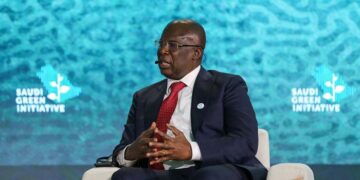 Timipre Sylva speaking on stage at the Saudi Green Initiative forum, seated in a chair wearing a dark suit and red tie with branded backdrop behind him