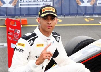 Nigerian-American racing driver Ugo Ugochukwu in white race suit and Pirelli cap celebrating Formula Regional Oceania Championship beside his car