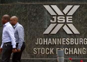 Two men walking past the Johannesburg Stock Exchange building with the JSE logo mounted on a stone wall in Johannesburg, South Africa