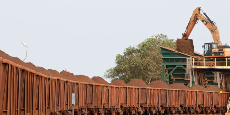 Excavator loading iron ore into railway wagons at a mining site in Liberia during large-scale export operations.