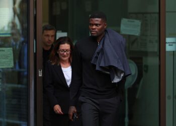 A professional footballer leaving a London court building alongside a woman, dressed in dark clothing