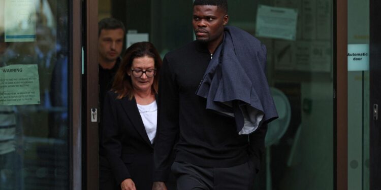 A professional footballer leaving a London court building alongside a woman, dressed in dark clothing