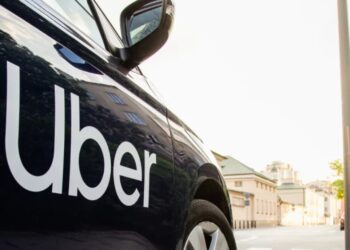 Close-up of a black Uber-branded car parked on a city street as pedestrians walk past, symbolising Uber’s exit from Tanzania