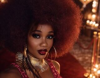 Woman with natural afro hairstyle wearing gold statement jewellery and red evening couture at a luxury fashion setting
