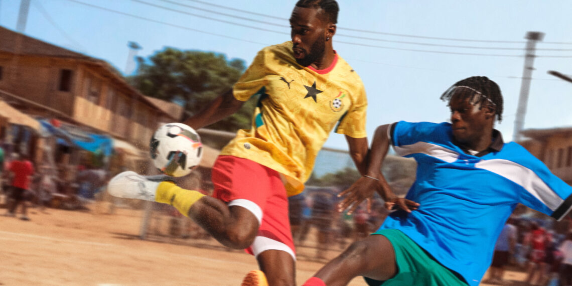 Ghana player in gold Away kit challenges for ball during fast-paced street football match in African urban setting