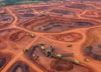 Aerial view of a large bauxite mine in Guinea with haul trucks and conveyor systems operating across red earth open-pit mining sites