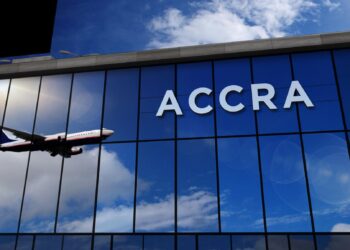 Passenger aircraft approaching Accra airport with terminal glass facade reflecting sky