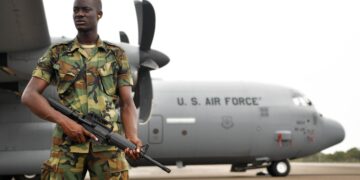 Ghanaian soldier standing guard beside a US Air Force military aircraft on an airport runway