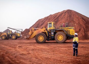 Heavy machinery loads bauxite at a mining site in Guinea, with large red ore stockpiles in the background