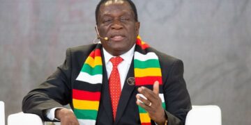 Zimbabwe President Emmerson Mnangagwa speaking at a public event, wearing a national flag scarf and suit