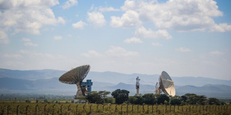 Satellite dishes in rural Kenya transmitting signals across a remote landscape with mountains in the background