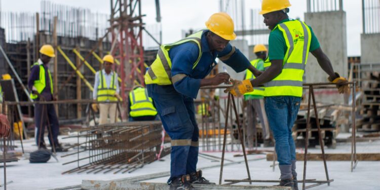 Construction workers in safety gear assembling steel reinforcement on a building site, highlighting manual labour conditions in Nigeria
