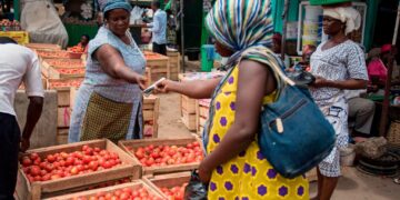 Woman buys tomatoes at a busy open market in Ghana as food prices rise amid inflation pressures