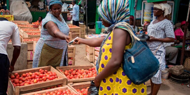 Woman buys tomatoes at a busy open market in Ghana as food prices rise amid inflation pressures
