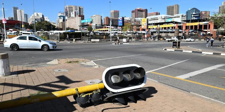 A fallen traffic light lies on a Johannesburg pavement with the city skyline visible in the background, symbolising growing infrastructure and governance challenges in South Africa’s financial hub