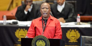 Julius Malema wearing a red EFF uniform while addressing South Africa’s parliament from a podium