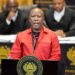 Julius Malema wearing a red EFF uniform while addressing South Africa’s parliament from a podium