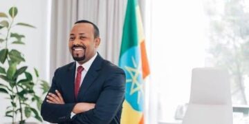 Ethiopian Prime Minister Abiy Ahmed standing in an office with arms crossed, with the Ethiopian flag visible behind him