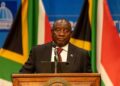 South African President Cyril Ramaphosa speaks at a podium with national flags behind him amid renewed political pressure over the Farmgate scandal