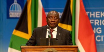 South African President Cyril Ramaphosa speaks at a podium with national flags behind him amid renewed political pressure over the Farmgate scandal