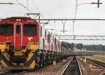 Freight train carrying cargo on South Africa rail line under overhead power infrastructure