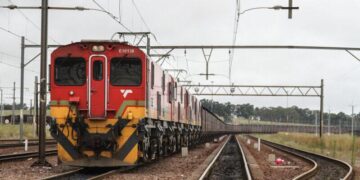 Freight train carrying cargo on South Africa rail line under overhead power infrastructure