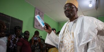 Cameroonian opposition figure Issa Tchiroma Bakary holds up a ballot paper after voting at a polling station during the 2025 presidential election, as journalists and observers watch
