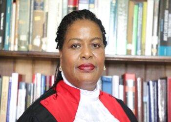 Justice Njoki Ndung'u, a judge of Kenya's Supreme Court, speaks at a podium bearing the Kenyan coat of arms during an official event, wearing judicial robes with Kenyan flags displayed in the background