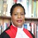 Justice Njoki Ndung'u, a judge of Kenya's Supreme Court, speaks at a podium bearing the Kenyan coat of arms during an official event, wearing judicial robes with Kenyan flags displayed in the background