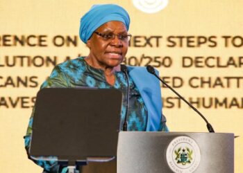 Namibian President Netumbo Nandi-Ndaitwah speaking at a podium during the Next Step: High-Level Consultative Conference on Reparatory Justice in Accra, Ghana. She is wearing a blue headscarf and addressing delegates from behind a lectern bearing Ghana's presidential seal