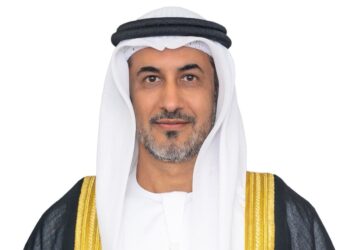 Portrait of Saeed bin Mubarak Al Hajeri, UAE Minister of State at the Ministry of Foreign Affairs, wearing a white kandura and ghutra with a black bisht trimmed in gold, facing the camera against a light grey background