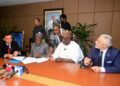 Officials from Africa Finance Corporation and Dangote Group representatives sit around a conference table during a document-signing ceremony, with media microphones in the foreground and staff observing in the background