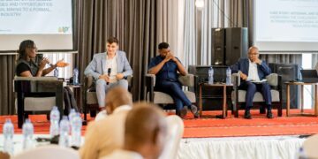 Panel discussion at an investment and mining conference in Kinshasa, Democratic Republic of Congo, featuring four speakers on stage discussing artisanal and small-scale mining reforms, with attendees seated in the foreground