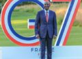 Kenyan President William Ruto stands in front of a large G7 summit installation in France, posing on a lawn during the 2026 gathering of world leaders