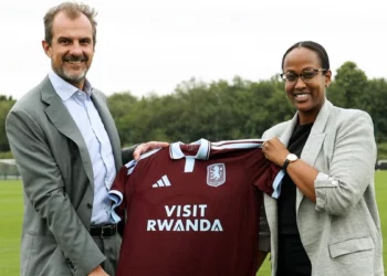 Aston Villa and Visit Rwanda representatives hold a claret football shirt displaying the Visit Rwanda front-of-shirt logo