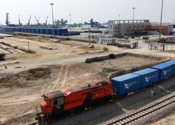 A red locomotive carries mineral freight containers through the Lobito railway terminal in Angola