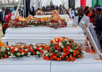 Rows of flower-covered white coffins are displayed during a memorial service for the victims of the Utumishi Girls' Academy dormitory fire in Gilgil, Kenya, as clergy, mourners and officials gather to pay their respects