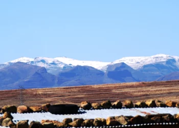 Snow-capped Maloti Mountains behind farmland and corrugated rooftops in Lesotho
