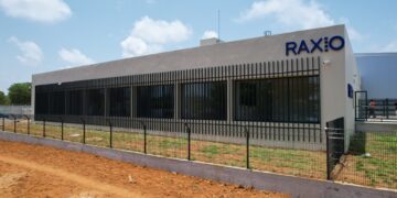 Exterior of a Raxio data centre building with secure perimeter fencing and the company’s logo displayed on the façade